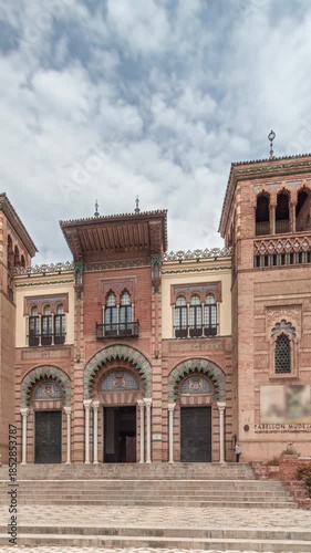 Facade of the Museum of Arts and Traditions of Seville in Maria Luisa Park. Mudejar-style building located across Plaza de America. Timelapse hyperlapse under cloudy sky. Seville, Spain.
