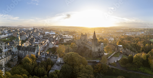 Aerial view of Dunfermline Abbey and Palace steeped in golden sunlight, with autumn trees contrasting against the ancient stone, Dunfermline, Scotland, United Kingdom.