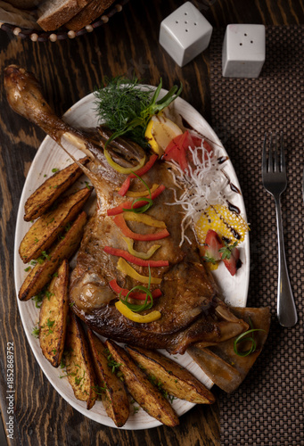 Roasted leg of lamb with potatoes and vegetables on a wooden background.