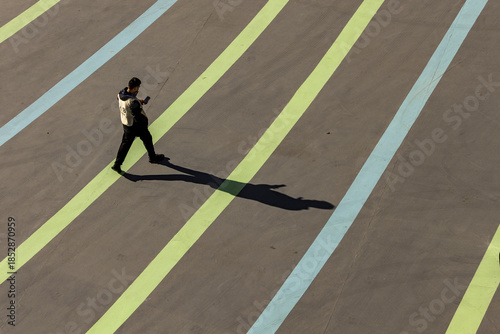 View of a lone figure casting a long shadow as he walks across a striped ground, bathed in harsh sunlight, contrasting with the cool blues and greens, Beijing, Beijing, China.