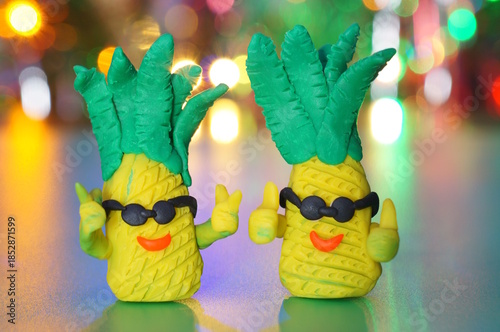 Toy pineapples made of plasticine on the background of a glowing garland. Festive mood.