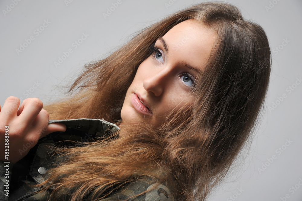 Fototapeta premium Porträt einer jungen Frau mit langem Haar und intensivem Blick vor hellem Hintergrund. Die natürliche Pose und der direkte Ausdruck vermitteln Selbstbewusstsein, Ruhe und moderne Porträtästhetik.