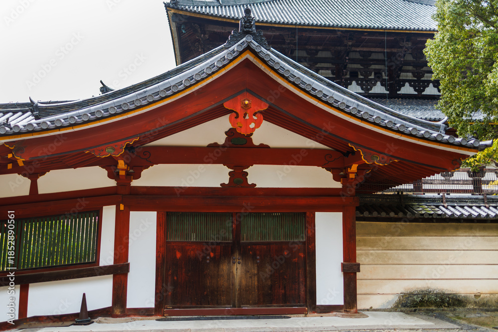 Fototapeta premium Serene Japanese Temple Corridor With Red Wooden Columns, Traditional Rooflines, And Lush Surroundings. Nara City, Japan