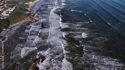 Aerial view of waves crashing on a sandy beach with rocky outcrops and lush green vegetation, Cape Town, Western Cape, South Africa.