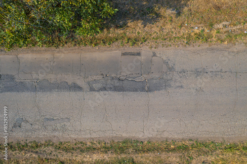 Cracked asphalt road surface with damaged patches and dry roadside grass