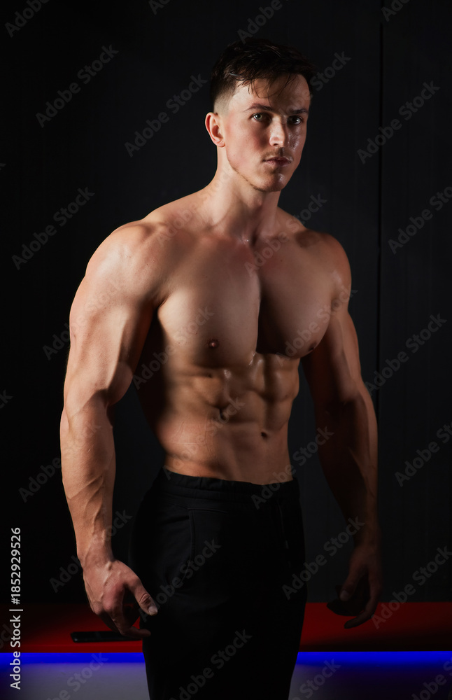 Obraz premium Portrait of a sweaty muscular bodybuilder posing on black background.