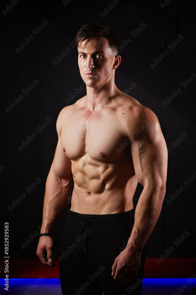 Fototapeta premium Portrait of a sweaty muscular bodybuilder posing on black background.
