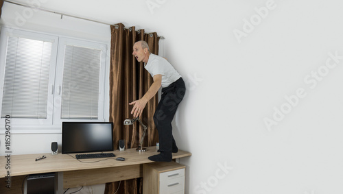 Senior citizen fixing curtain rod. Pensioner standing on the desk. Home accident