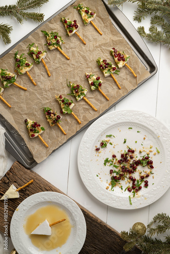 Tree shaped brie cheese appetizers with pomegranate, walnuts, cilantro and a pretzel stick, vertical.