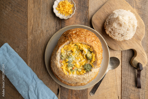 Broccoli cheddar soup in a sourdough bread bowl on wooden table with blue napkin and antique spoon.
