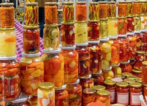 Homemade colorful pickled vegetables inside closed glass jars sold on market stall