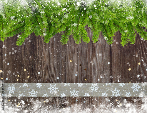 Christmas or New Year greeting card. Branches of spruce and ribbon with snowflakes and golden stars on snowbound wooden background.