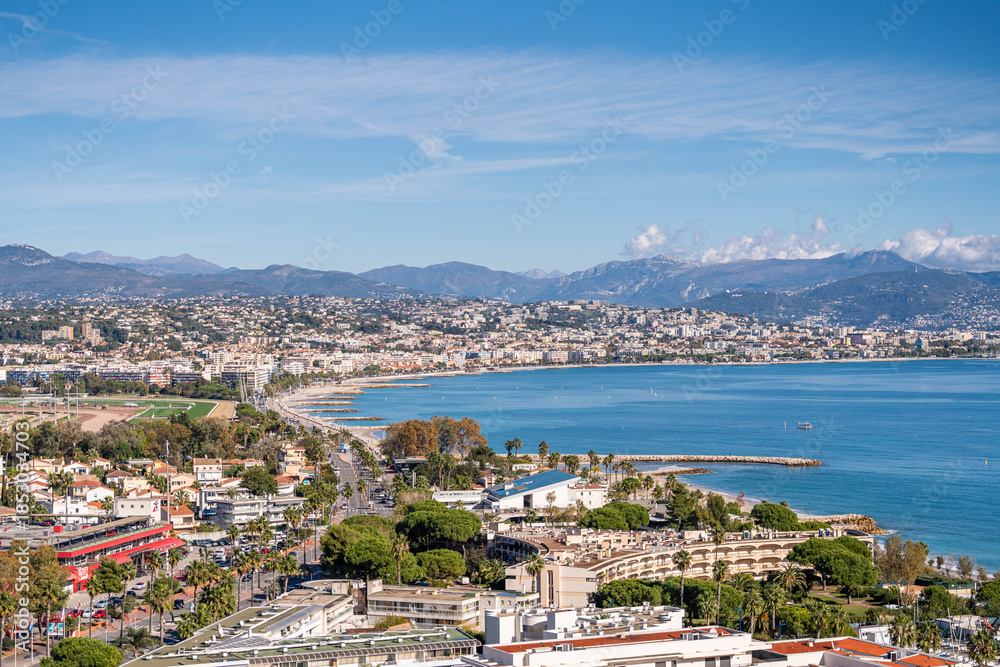 Fototapeta premium Panoramic coastal city view with blue sea, urban shoreline and distant mountains under clear sky