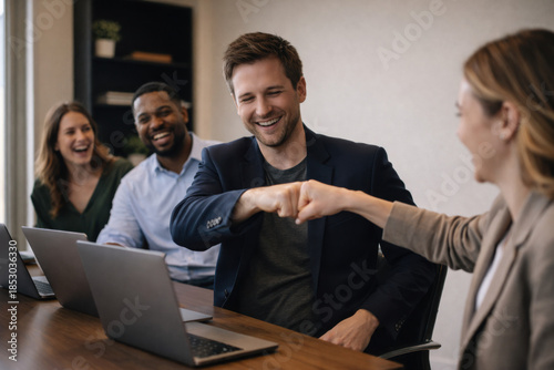 Colleagues celebrating business success with friendly fist bump in modern office