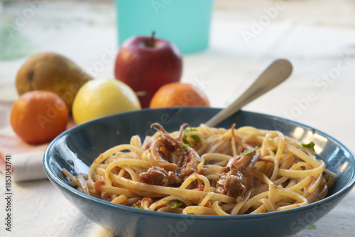 spaghetti with squid ragu sauce in blue dish with fresh fruit on the background