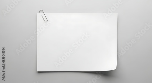 A white paper sheet, held by a metal clip, partially curled, against a gray background. Simple, clean, and minimalist composition
