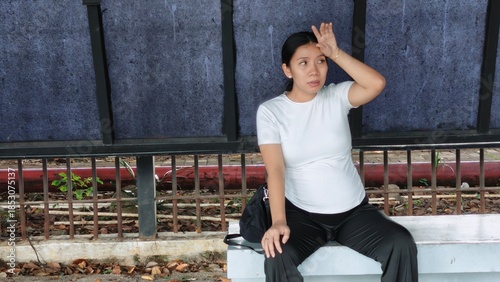 A tired pregnant woman sitting at a modern city bus shelter, looking exhausted while waiting for public transport
