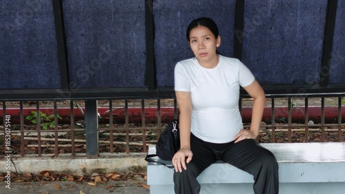 A tired pregnant woman sitting at a modern city bus shelter, looking exhausted while waiting for public transport