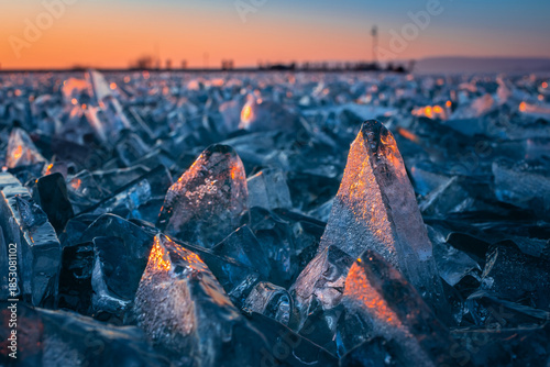 Fonyod, Hungary - Transparent ice cubes on the frozen Lake Balaton on a cold winter afternoon with golden sunset lights and Fonyod pier at background out of focus