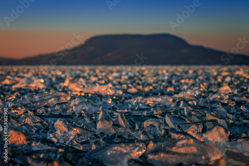 Fonyod, Hungary - Panoramic view of the frozen Lake Balaton on a cold winter afternoon with golden sunset lights and Badacsony mountain at background out of focus