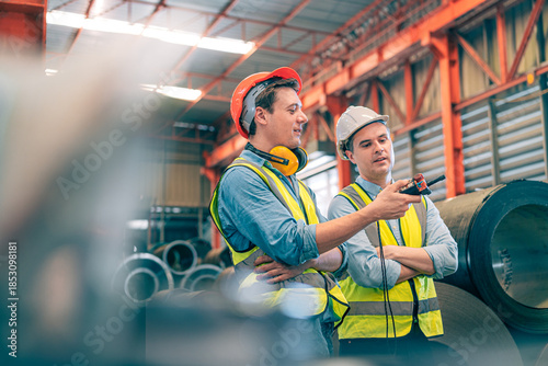 Caucasian industrial engineer men controlling overhead crane with remote in factory. Worker partner wear safety helmet vest lifting heavy metal coil material. Manufacturing hoist machine logistics