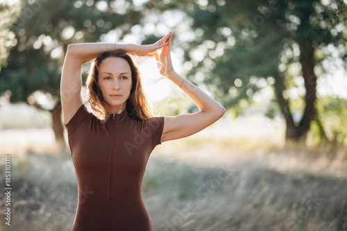 A woman practices a calm stretching pose outdoors, surrounded by trees and soft natural light, creating a peaceful and balanced atmosphere.