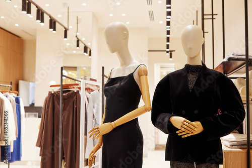 Two contemporary mannequins with wooden articulated arms showcase fashionable black dresses and blouses on display in a stylish retail clothing store environment