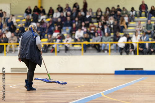 Person cleaning gymnasium court floor during event