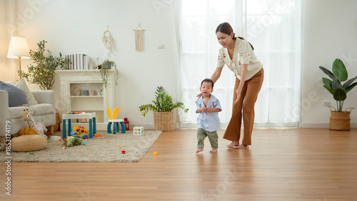 Boy Takes His First Steps at Home While Holding His Mother's Hand in a Warm Living Room Setting