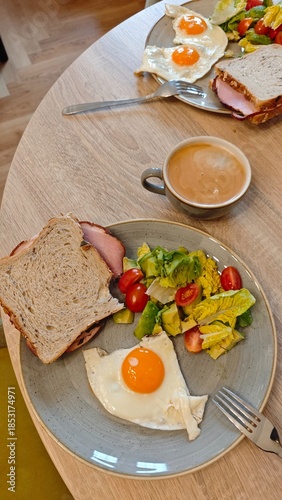 Plate with fried egg sandwich fresh salad and coffee served on a wooden table in a cozy cafe interior. The image represents balanced breakfast routine relaxed dining and healthy morning lifestyle