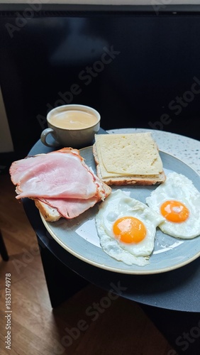Plate with fried egg ham cheese sandwich and coffee served on a small table in a cozy cafe setting. The image represents classic breakfast routine, comfort food, and relaxed morning lifestyle