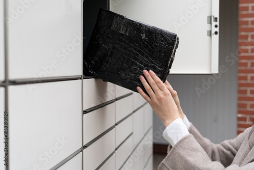 Person delivers a package to a mail locker during daytime in an urban setting with a simple design and organized layout
