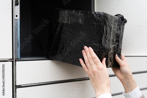 Delivery person places black package into secure locker at an urban location during afternoon hours