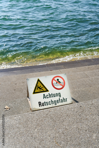 Warnschild mit der Aufschrift Achtung Rutschgefahr an den Treppenstufen der kleinen Seemole am Bodensee in Bregenz