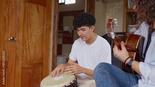 Teenager playing drum during music lesson with LGBTQ teacher playing guitar indoors
