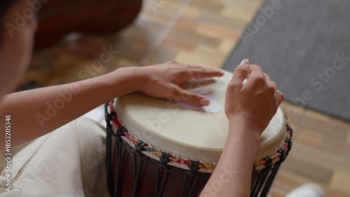 Close up of teenager hands playing a djembe drum instrument indoors