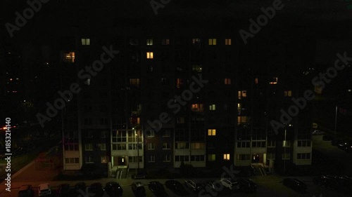 Transition from dusk late night over a high-rise apartment complex, showing windows take turns glowing and cars moving through the parking lot, and darkness descends on city's Time Laps neighborhood