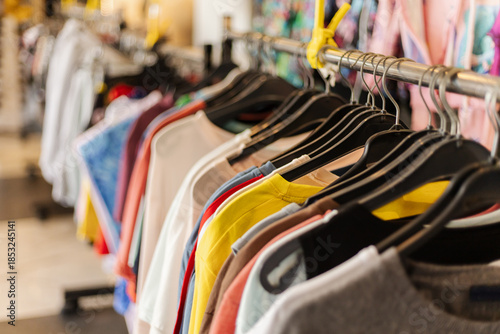 T-shirts of various colors hang on a rack inside a retail store. Shoppers browse the clothing while enjoying the busy atmosphere of the shop