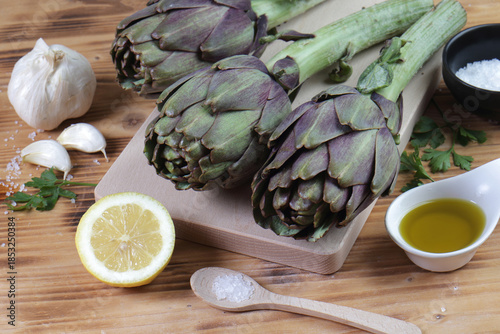  Fresh Artichokes on Cutting Board with Mediterranean Ingredients: Lemon, Garlic, and Olive Oil