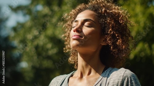 Medium shot of a person breathing deeply outdoors, shoulders relaxing, calm expression. Moment of release, mindfulness and stress relief in natural environment.