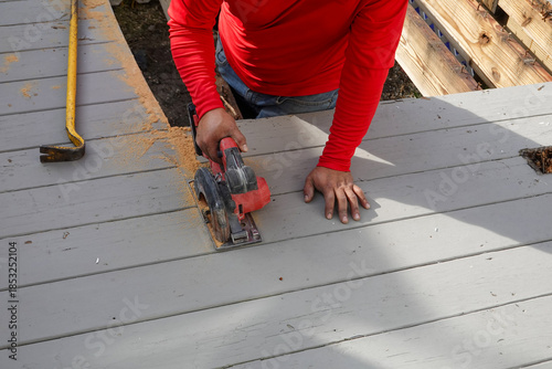 Carpenter cutting wooden planks on a deck with a circular saw