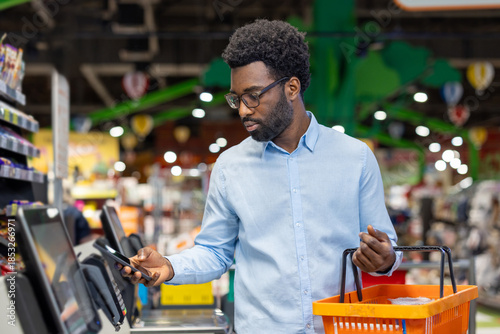 фотографія Man scanning groceries at a modern self-checkout terminal while using a smartpho