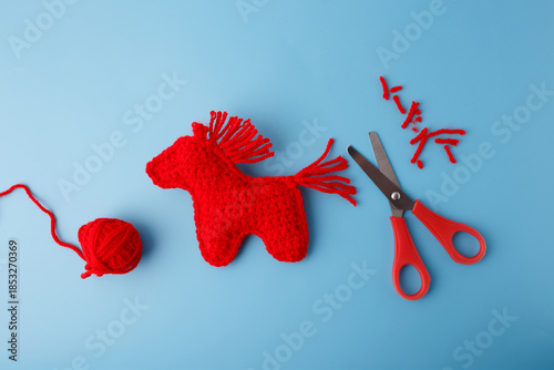 Fotografi Red crocheted horse with yarn ball and scissors, perfect for craft blogs, handma