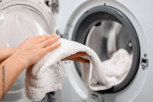 Hands of a woman holding a freshly laundered white towel, removing it from a modern washing machine, showcasing home laundry care and cleanliness in a bright environment
