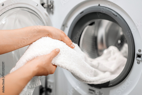 Hands of a person removing fluffy white towels from a modern dryer, showcasing laundry care and home maintenance in a bright, clean environment with soft textures