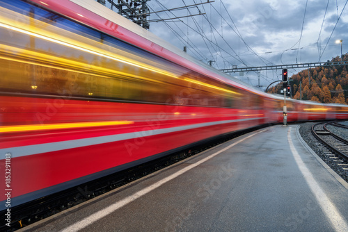Bilde på lerret Blurred red passenger train passing mountain railway station during rain in Swiss Alps at night