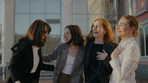 Group of friends share laughter outside a building during late afternoon in a social setting, enjoying their time together with smiles and conversations