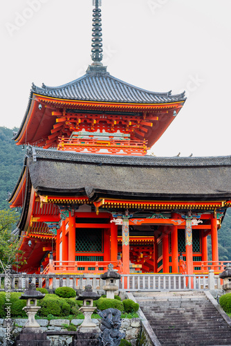 A stunning vermilion pagoda and traditional temple architecture stand against a lush mountain backdrop in Kyoto, Japan.