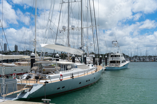 A sleek luxury yacht moored at Viaduct Harbour with the modern Auckland CBD skyline and clear blue sky in the background.