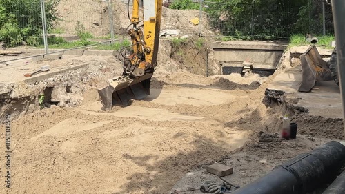 Excavator bucket spreads and levels sand at construction area. Process of preparing soil surface for further building works. Heavy machinery in action.